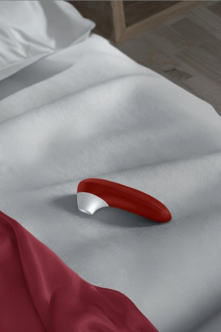 Aspirateur à clitoris rouge posé sur un lit aux draps gris